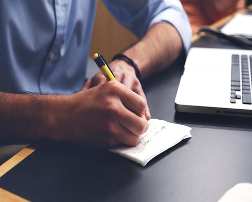 A desk with a notepad, a pen, and a laptop ready for writing