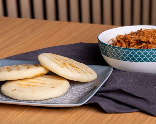 Table with traditional Colombian breakfast including arepa and hot coffee